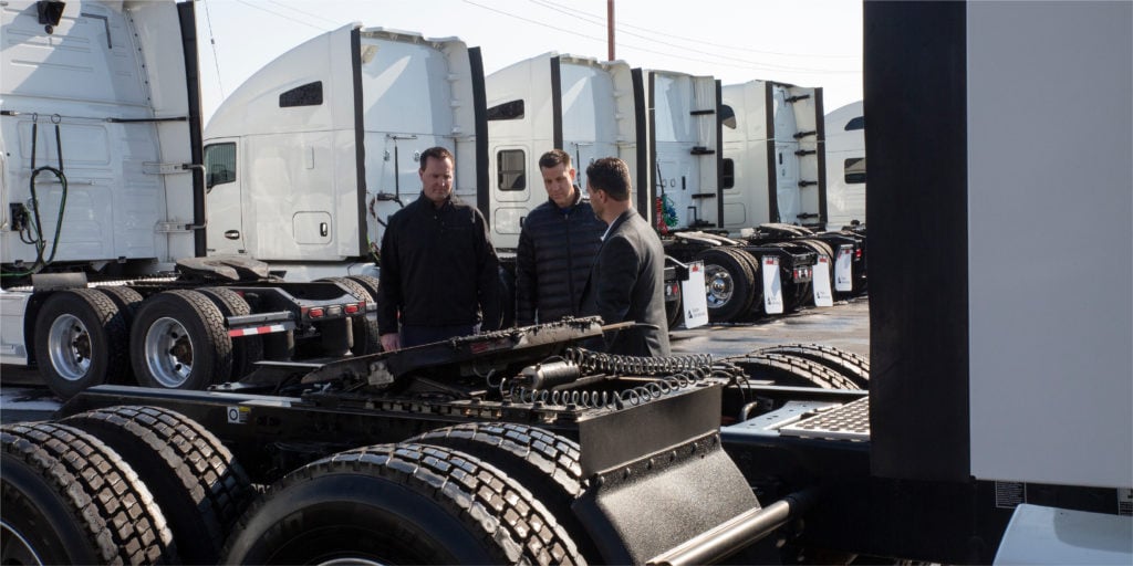 Three men talking near a truck and looking at wheels